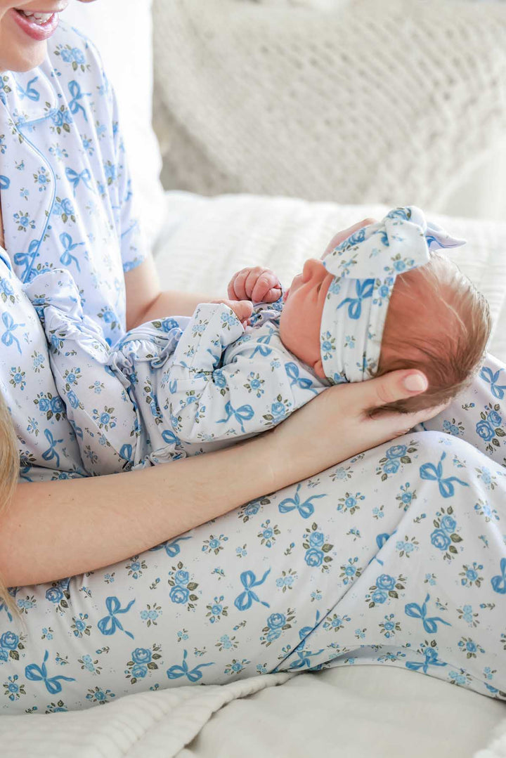 Mother in matching pajamas cradling her newborn, who wears a Tied In Blooms bow headwrap and swaddle in blue floral and bow print