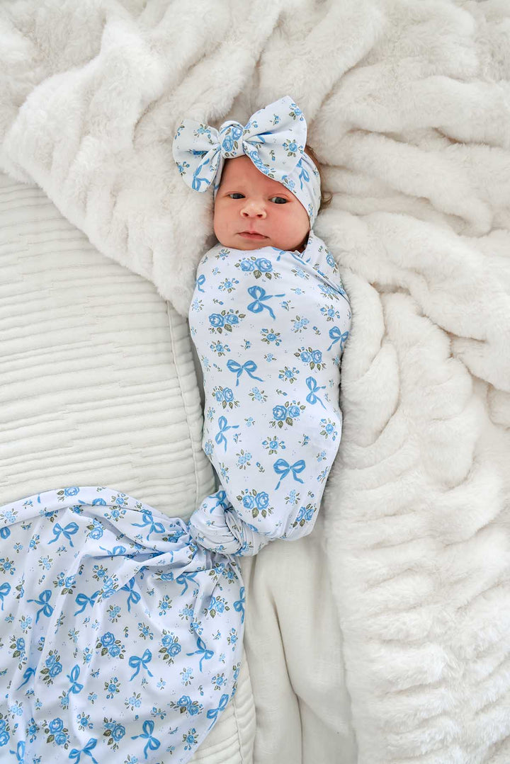 Newborn baby lying swaddled and wide awake, wearing a Tied In Blooms bow headwrap in blue floral and bow print