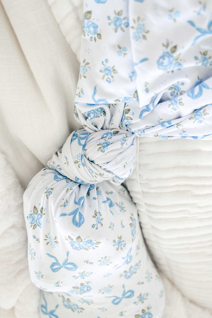 Close-up of a Tied In Blooms oversized swaddle blanket in blue floral and bow print, knotted at the end