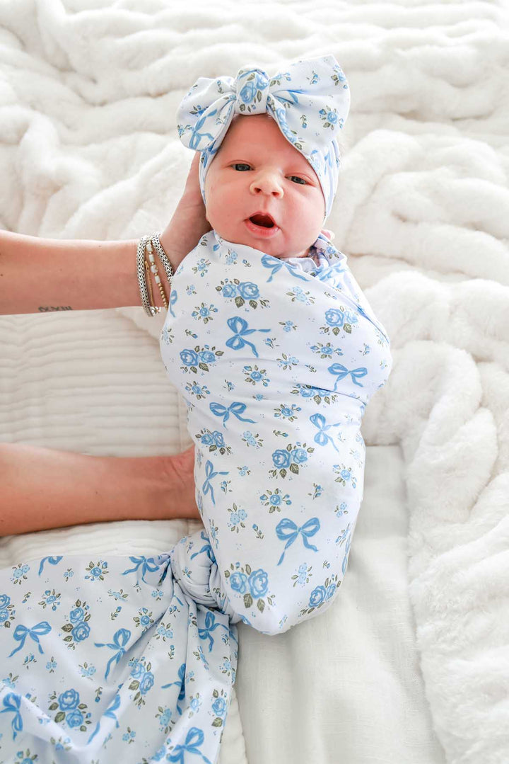 Newborn baby wearing a Tied In Blooms bow headwrap, swaddled in matching blue floral and bow print fabric
