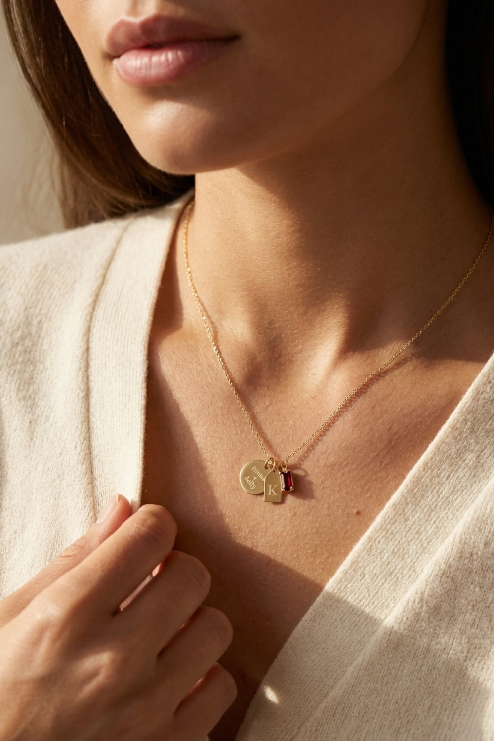 woman wearing engraved gold necklace with charms and red birthstone