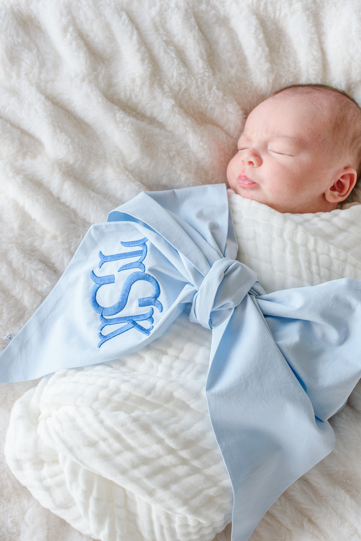 baby boy wrapped in white swaddle with light blue newborn bow sash wrapped around 