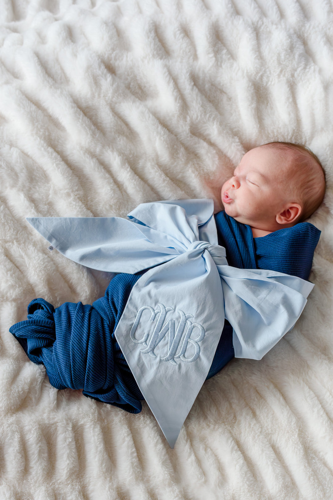 baby boy wrapped in navy swaddle blanket with light blue monogram bow sash wrapped around