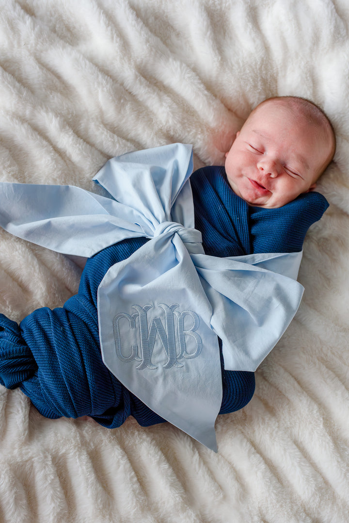 baby boy wrapped in navy blue waffle swaddle with monogrammed light blue sash wrapped around him