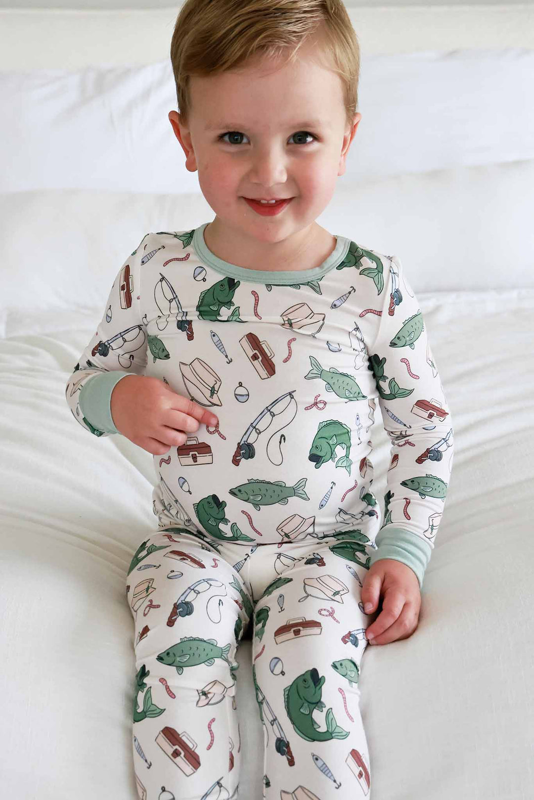 Toddler sitting and smiling wearing the Off The Hook two piece pajama set with fishing themed print