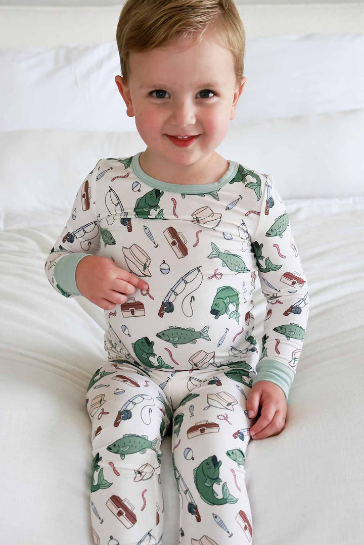 Toddler sitting and smiling wearing the Off The Hook two piece pajama set with fishing themed print