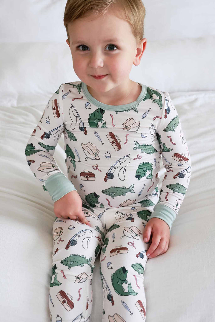 Close-up front view of toddler wearing the Off The Hook two piece pajama set with fishing print and sage green trim