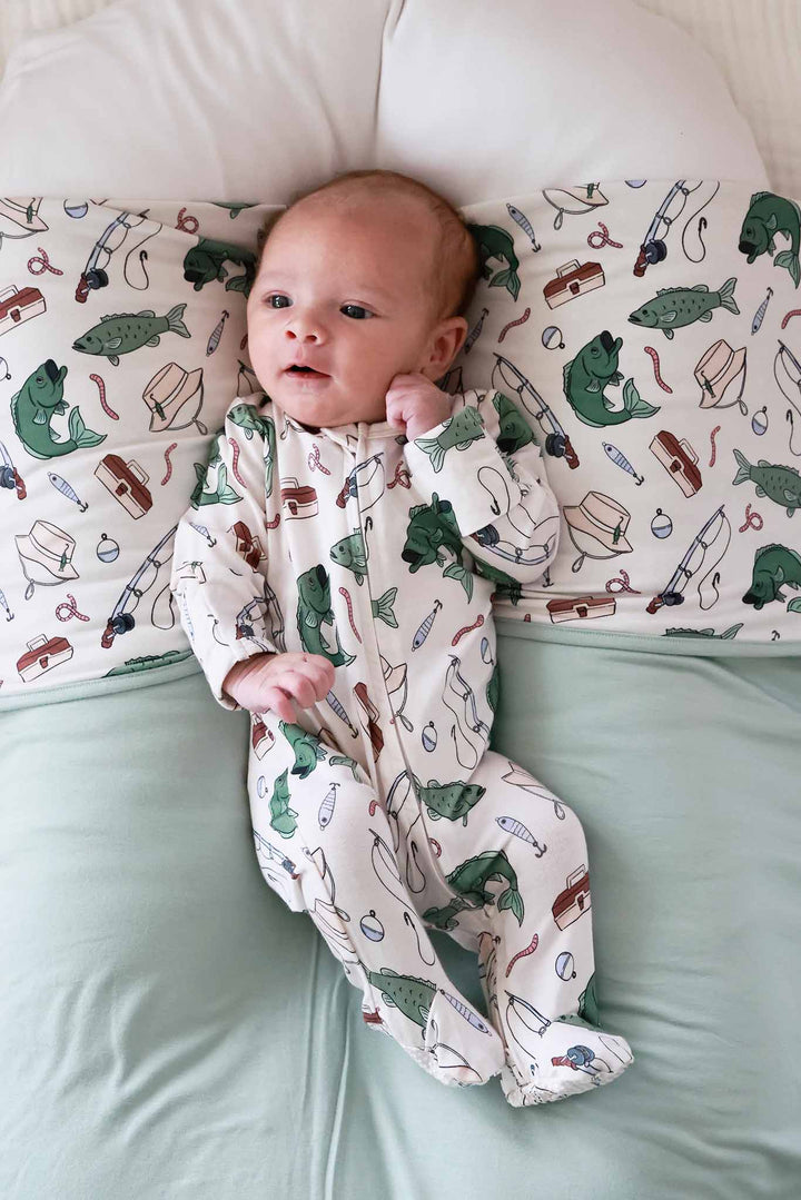 Newborn lying on bed wearing the Off The Hook zipper footie showing full length with fishing themed print