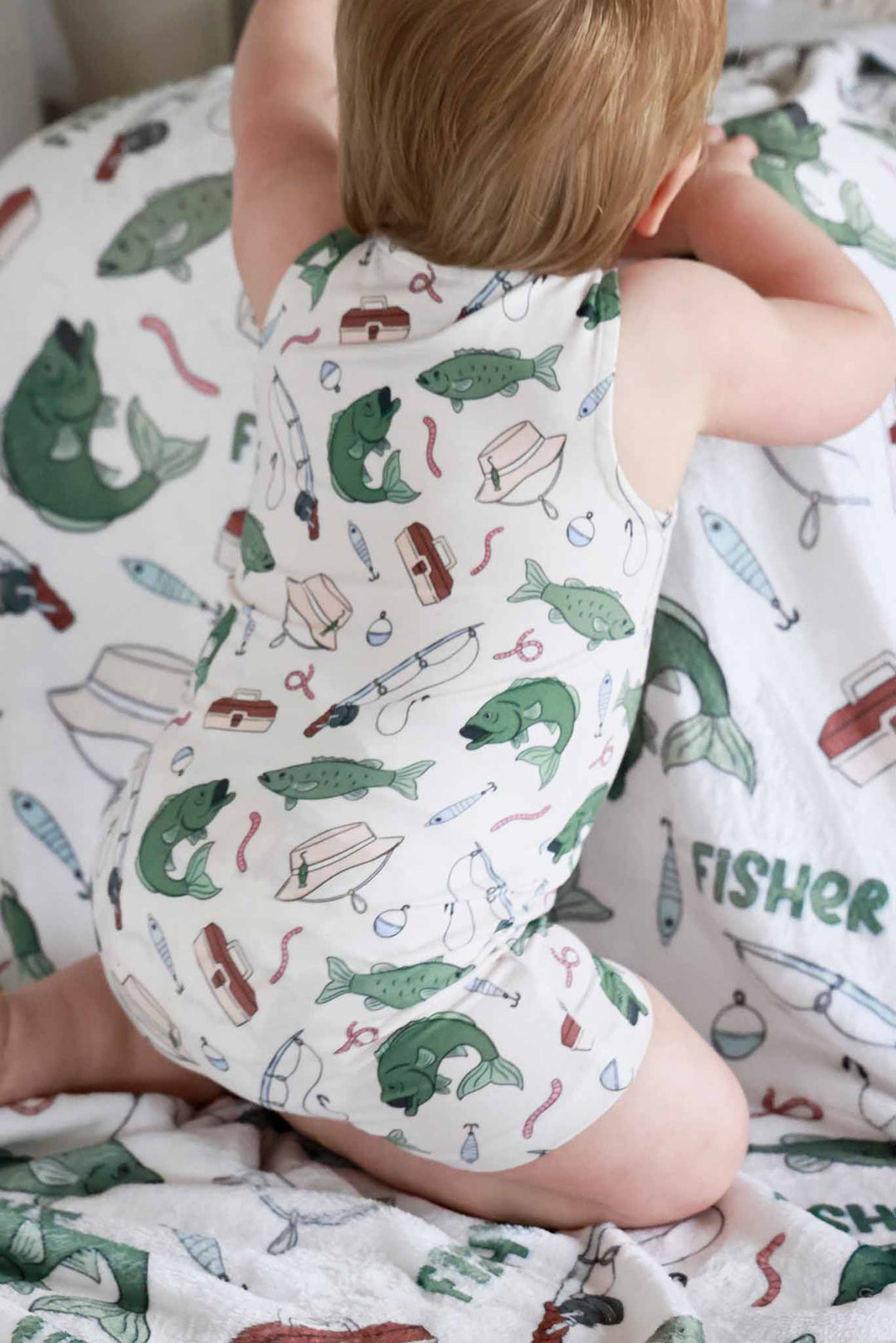 Baby showing the back of the Off The Hook sleeveless snap romper while sitting on fishing themed blanket