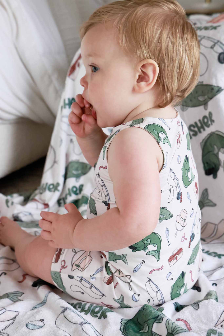 Baby sitting sideways wearing the Off The Hook sleeveless snap romper with fishing blanket in background