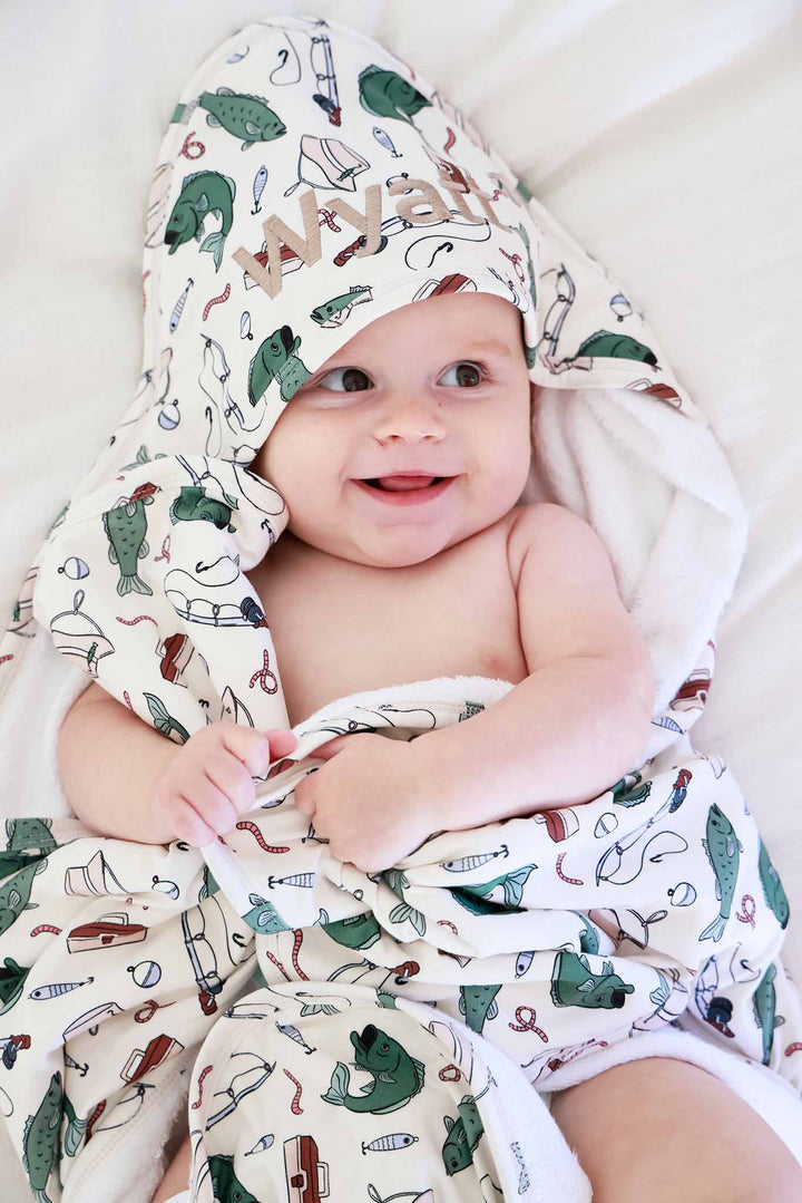 Smiling baby wearing the Off The Hook embroidered bamboo hooded towel with fishing themed print