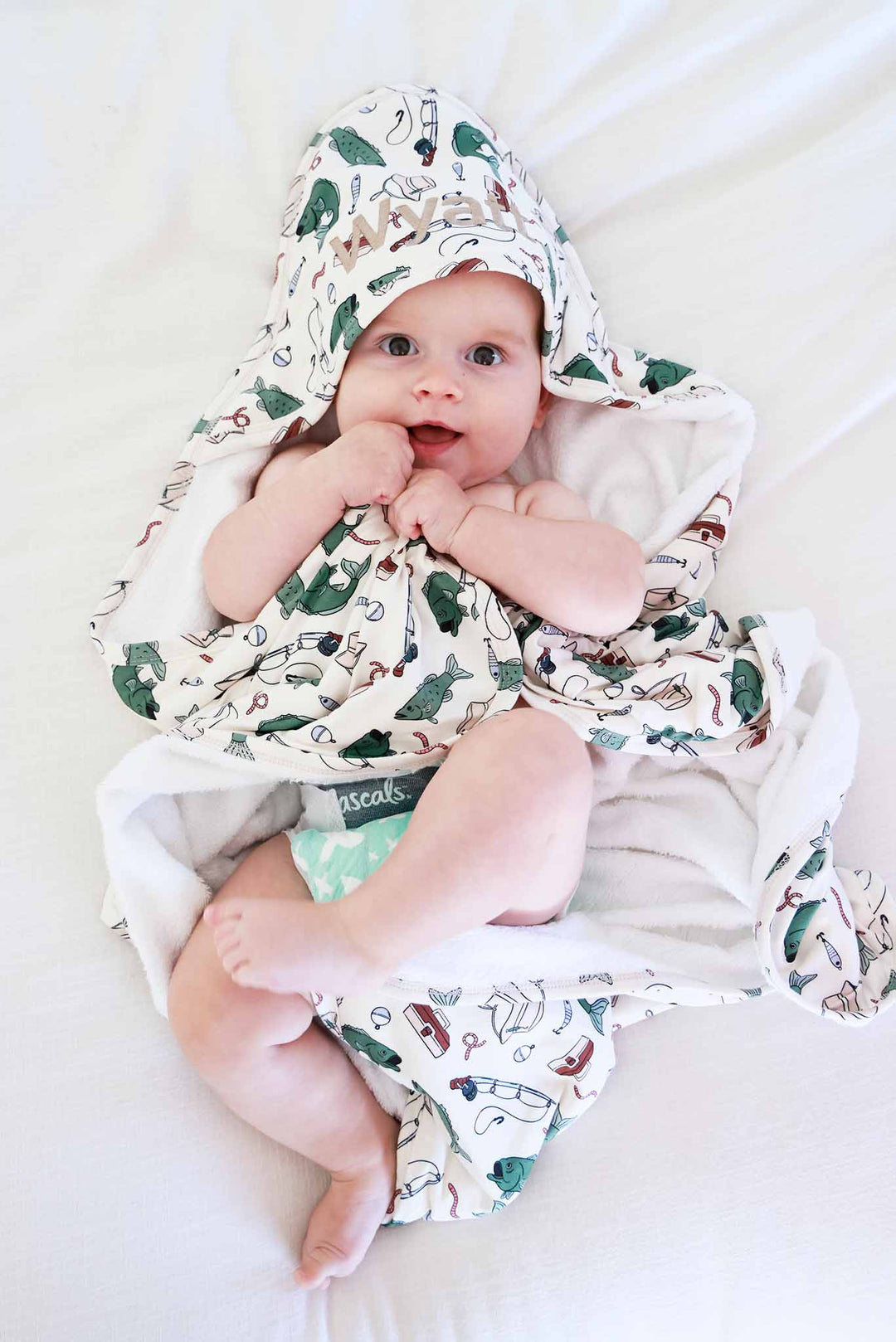 Overhead view of baby lying down wrapped in the Off The Hook bamboo hooded towel with fishing print