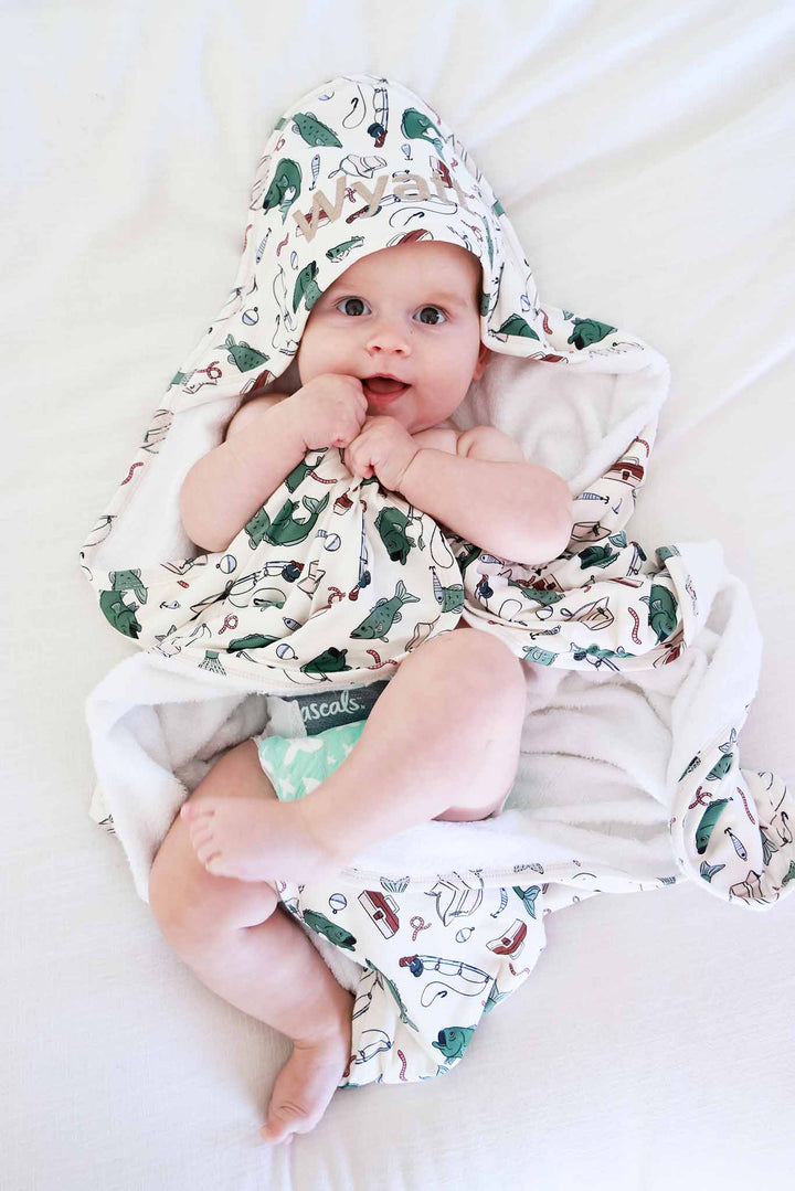 Overhead view of baby lying down wrapped in the Off The Hook bamboo hooded towel with fishing print