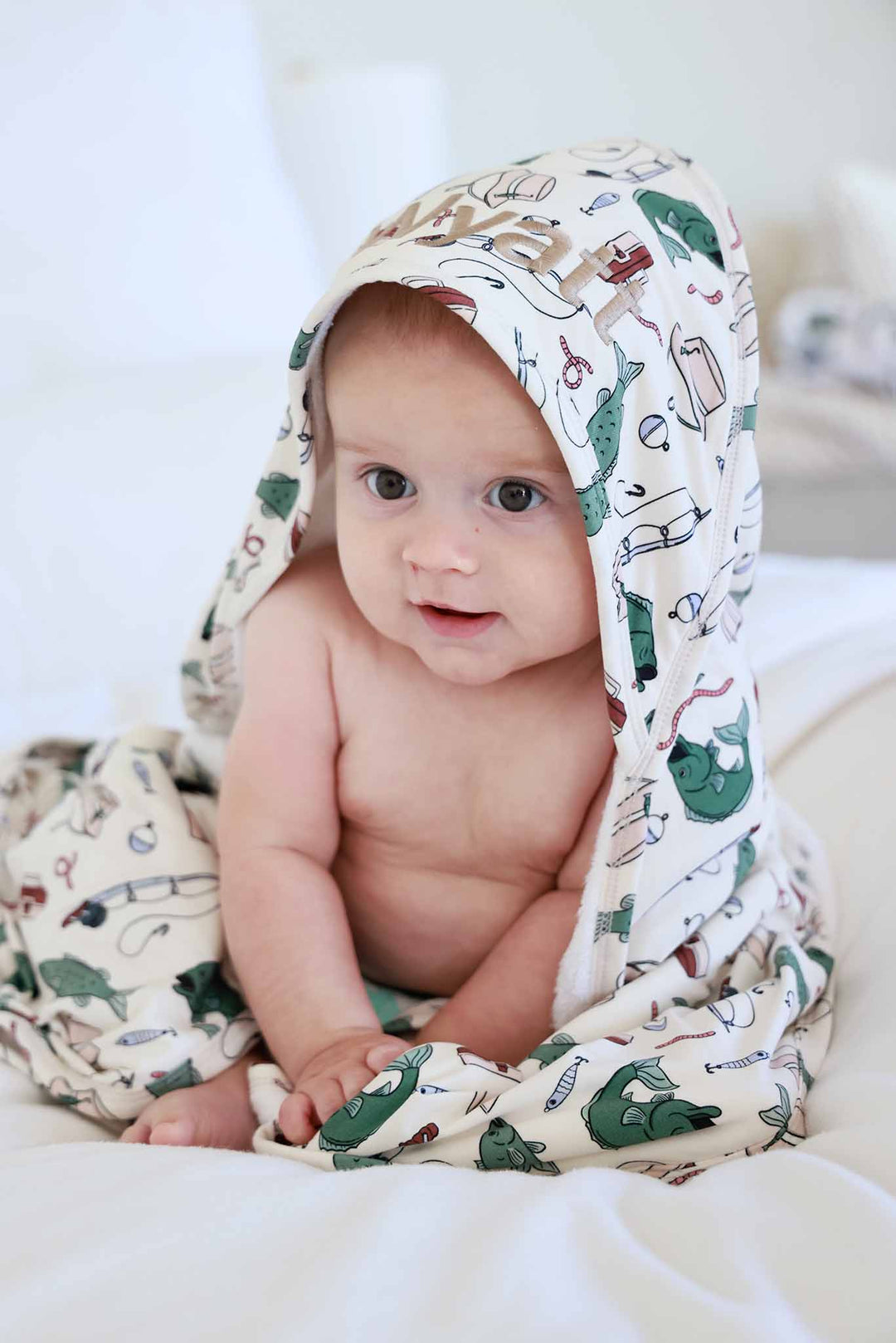 Baby sitting up wearing the Off The Hook embroidered bamboo hooded towel with fishing themed print