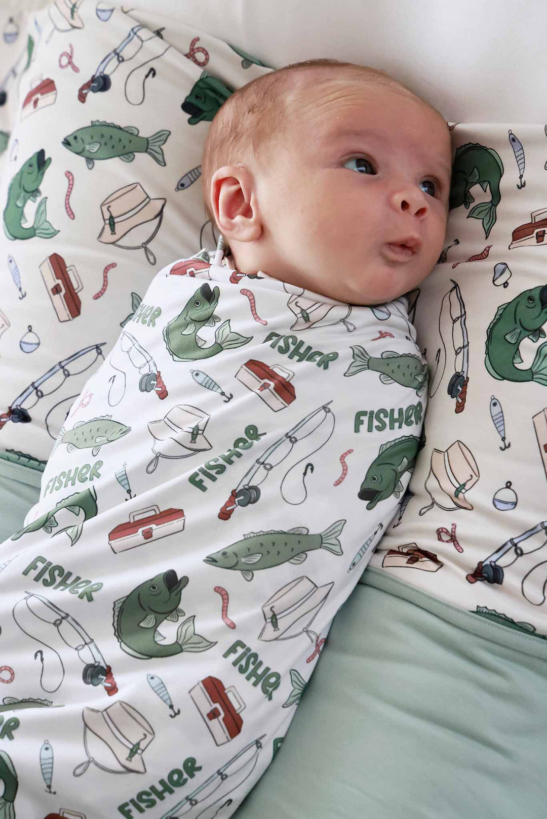 Newborn swaddled in the personalized Off The Hook swaddle blanket with fishing themed print lying on matching blanket