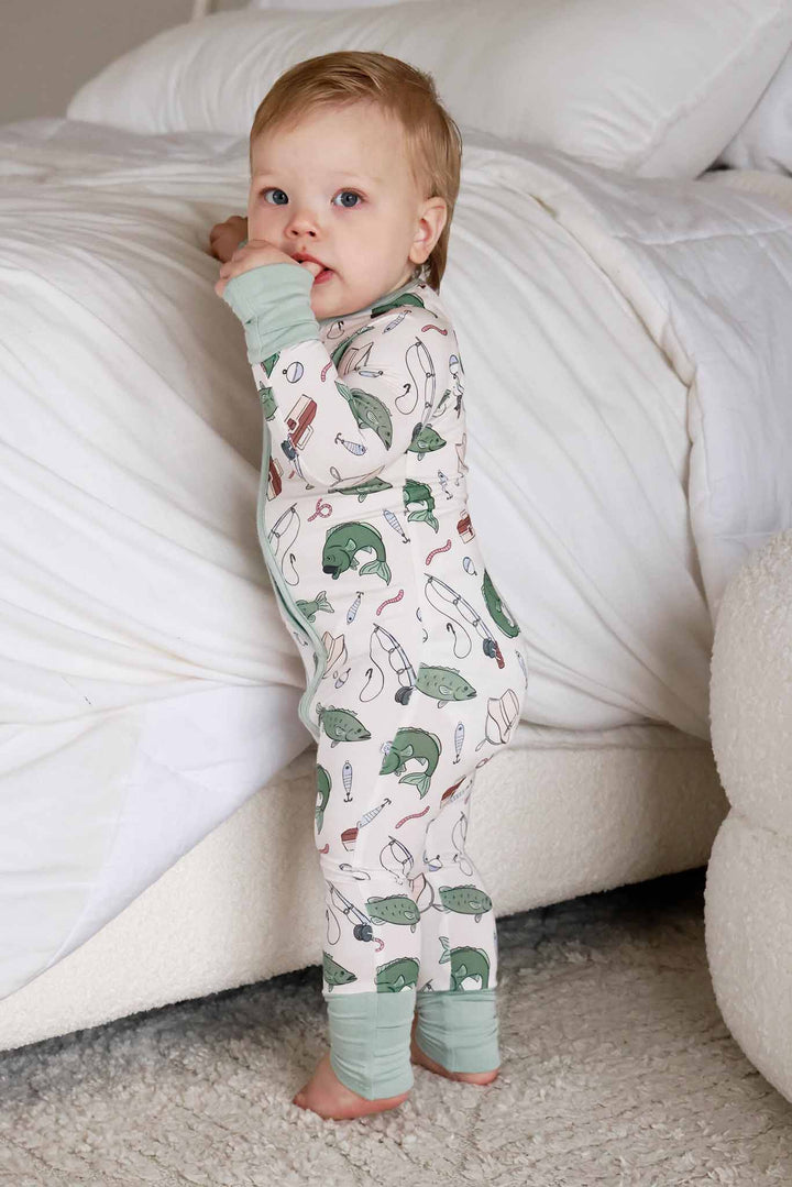 Baby standing next to couch wearing the Off The Hook convertible zip romper showing full length view
