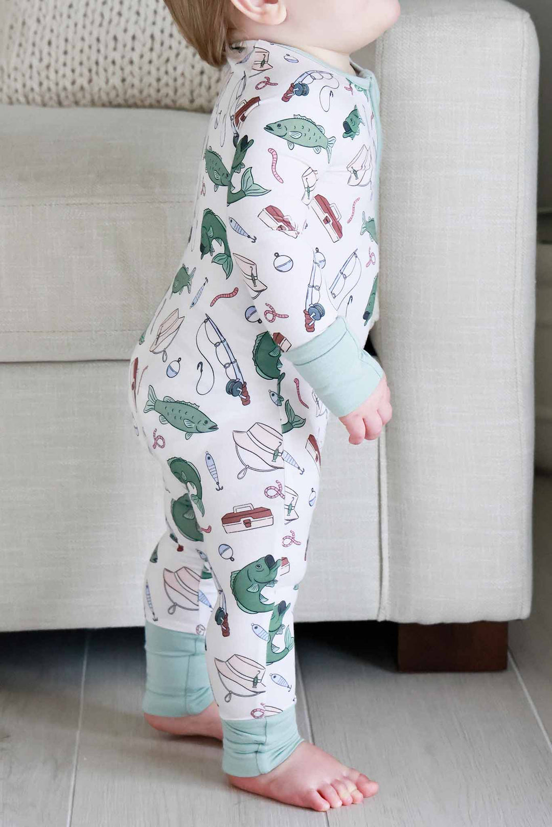 Side view of baby standing wearing the Off The Hook convertible zip romper with fishing print and sage green trim