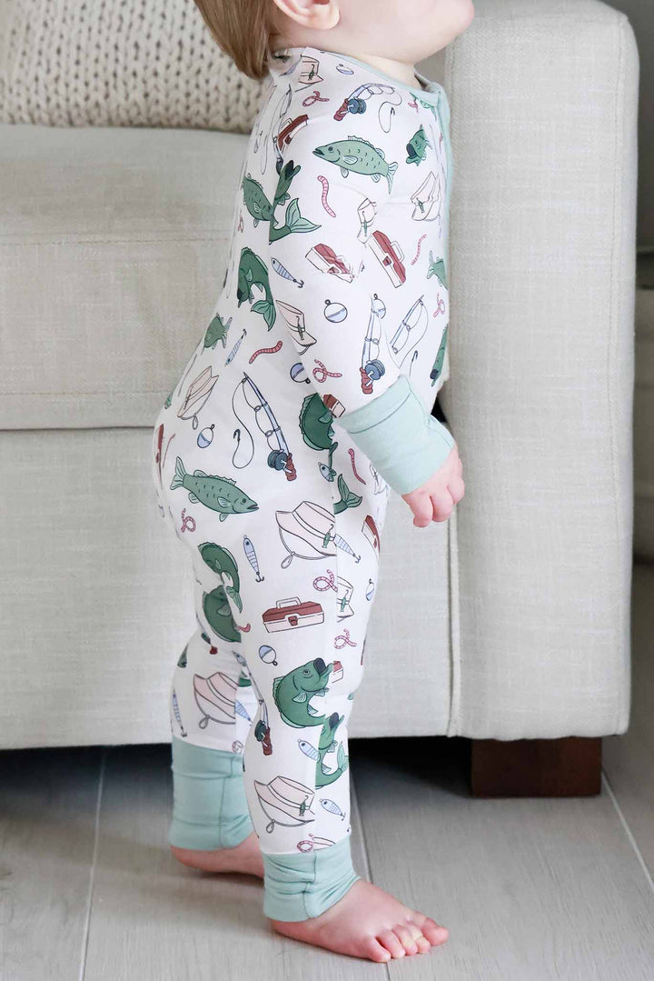Side view of baby standing wearing the Off The Hook convertible zip romper with fishing print and sage green trim