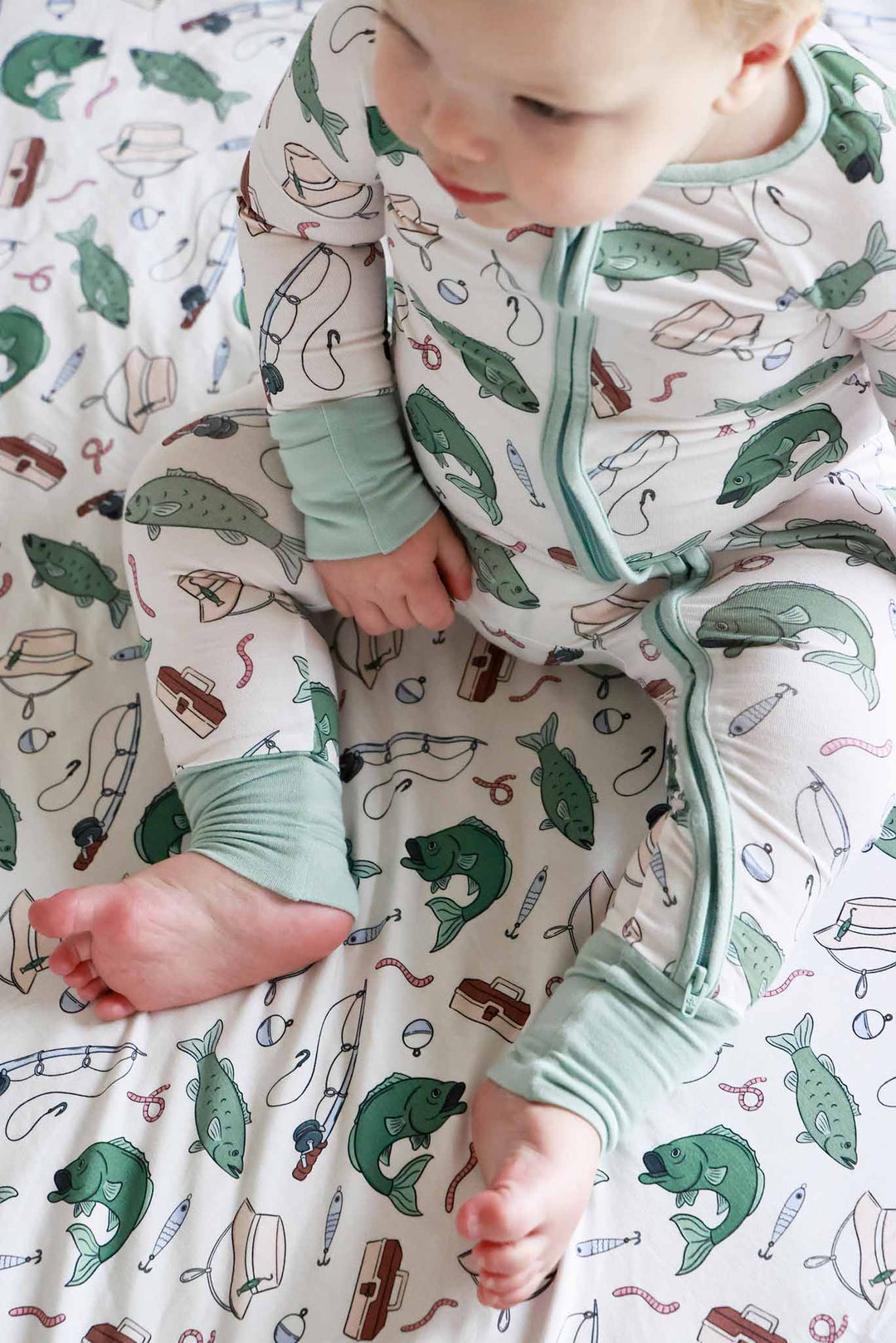 Overhead view of baby lying down in the Off The Hook convertible zip romper on fishing themed blanket