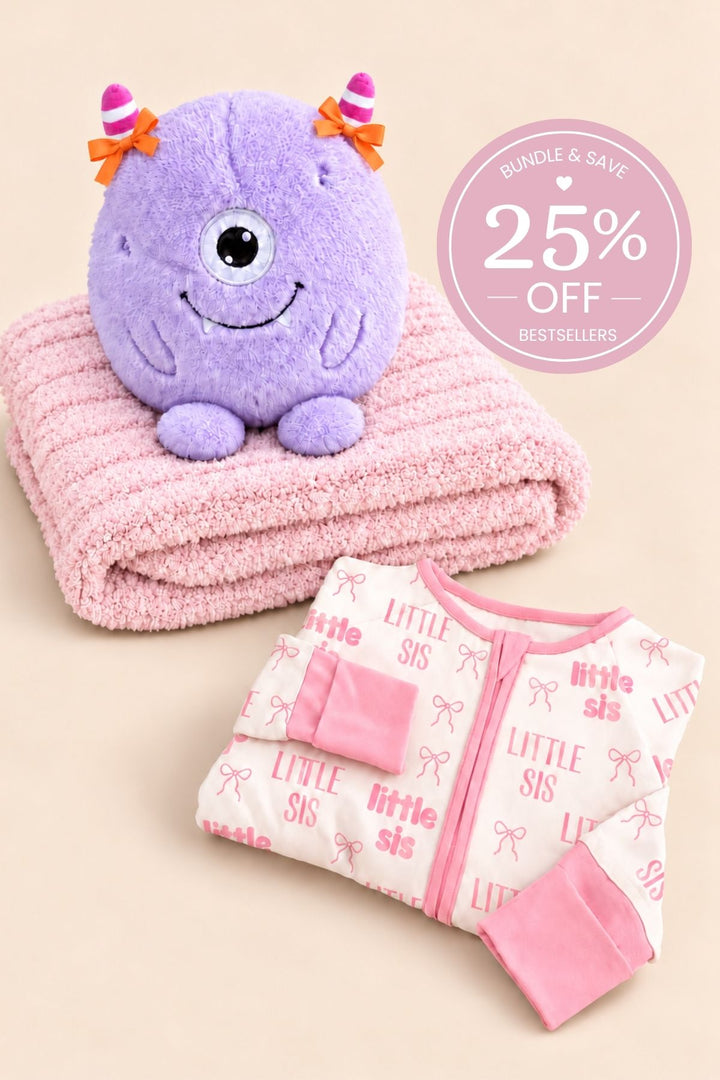 Hanger shot of a Caden Lane pink bamboo convertible zip romper in a Little Sis print featuring pink lettering and bows, paired with a purple monster plush and rose blanket.