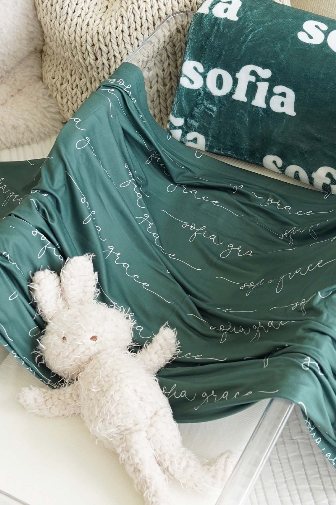 Green blanket with 'sofia' printed on it, draped over a surface with a white plush toy underneath.