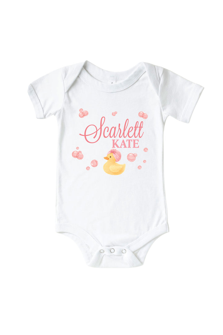 White baby bodysuit with personalized pink bubble duckie graphic featuring yellow rubber duck, pink bubbles, and custom name on front
