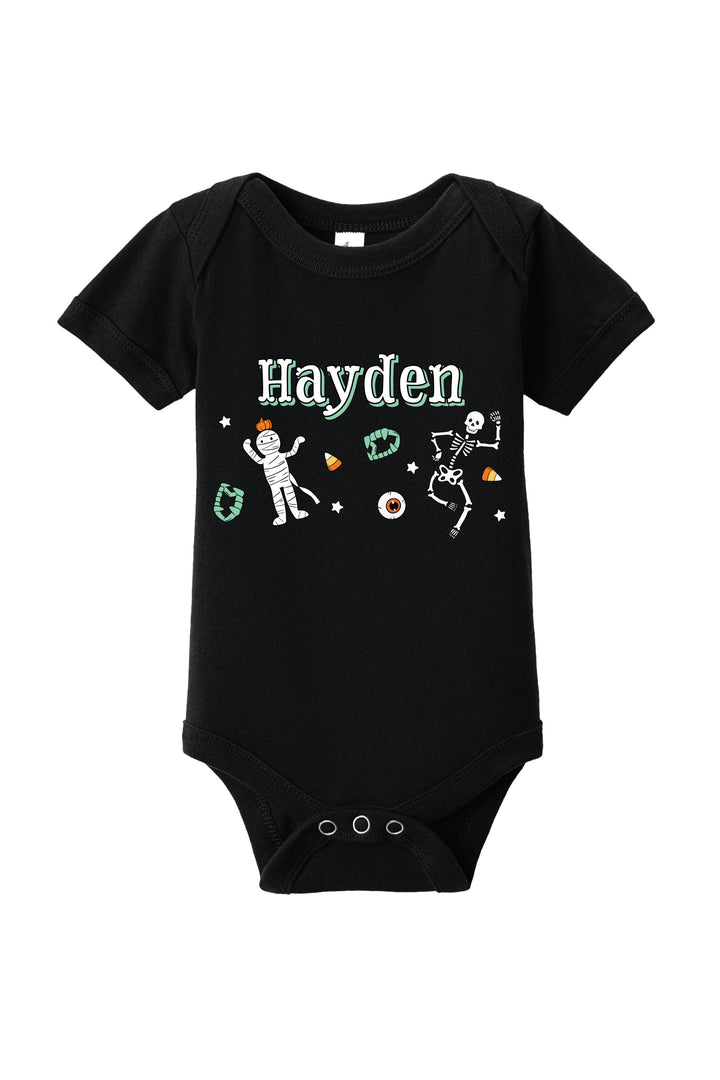 Black baby onesie personalized with the name 'Hayden' and Halloween graphics including dancing skeletons, an eyeball, and candy corn.