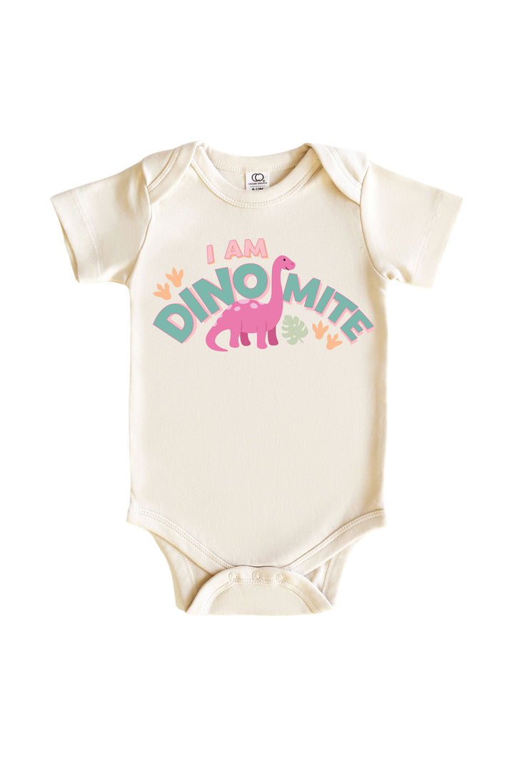 Natural cream baby bodysuit with I AM DINOMITE text in teal and pink lettering featuring a pink brontosaurus dinosaur graphic with colorful leaf accents
