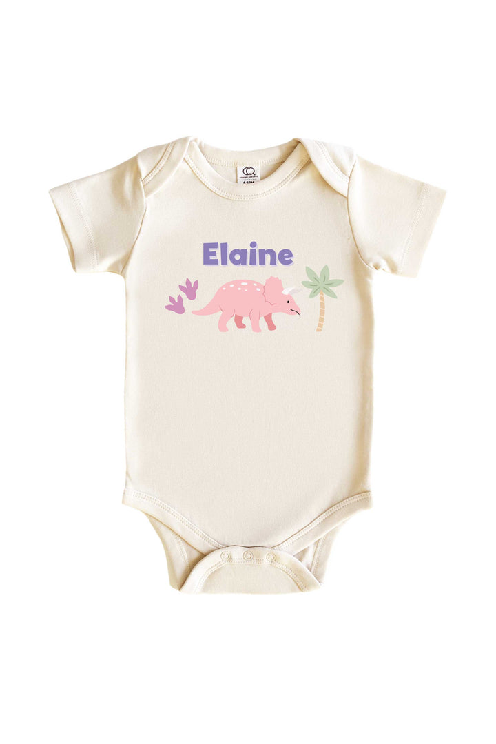 Natural cream baby bodysuit with personalized name in purple lettering and a pink triceratops dinosaur graphic with pastel plant accents