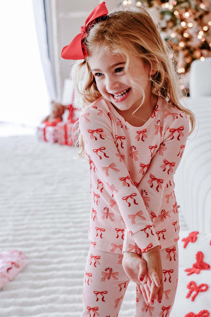 Smiling child wearing the Caden Lane Peppermint Bows Bamboo Waffle Two-Piece Pajama Set, made from soft bamboo viscose waffle knit with a festive bow and candy cane print for cozy Christmas pajamas.