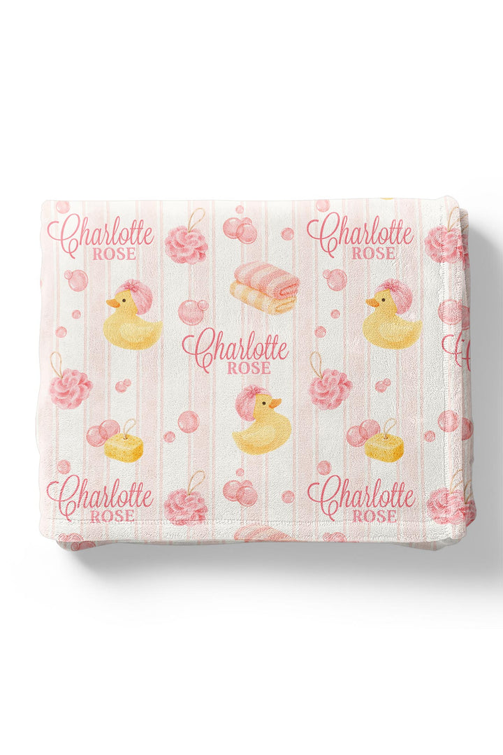 Folded pink Bubble Duckies personalized blanket showing yellow rubber duck, pink rose, and bubble print with custom name