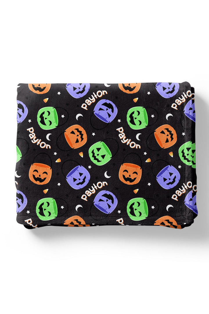 Folded personalized Halloween blanket with repeating name text and colorful jack-o-lantern candy bucket print