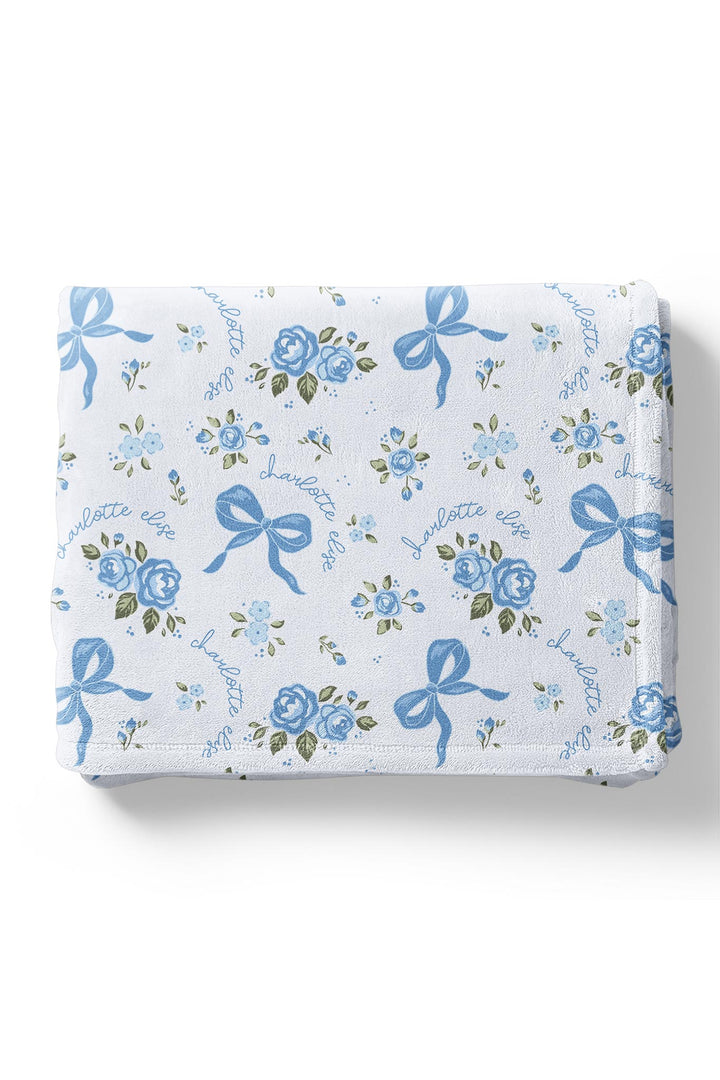 Folded Tied In Blooms blanket with blue floral and bow print, personalized with names embroidered in cursive script