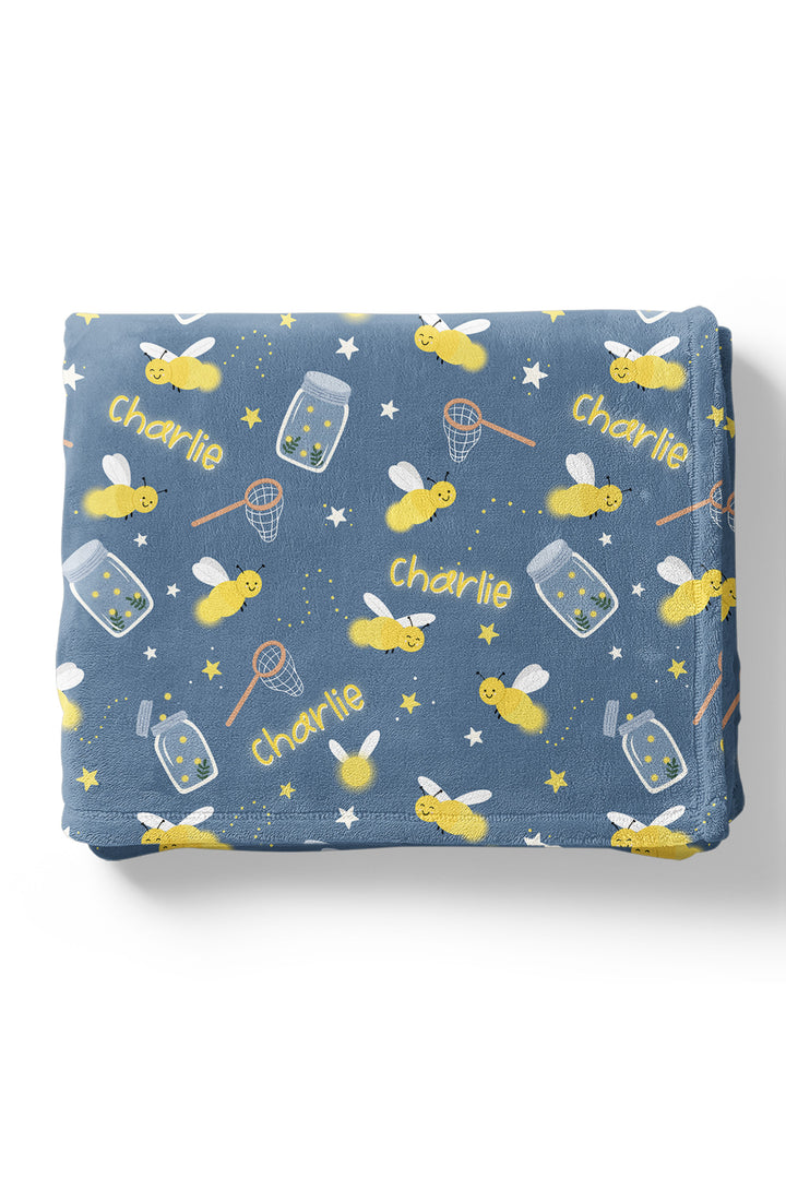 Product shot of a neatly folded Caden Lane blue plush personalized blanket in a Chasing Fireflies print featuring fireflies and mason jars, repeating the name "Charlie."