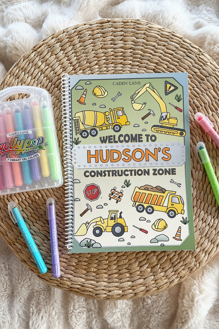 Caden Lane 'Welcome to Hudson's Construction Zone' coloring book on a woven tray with a fur throw, Gellypop gel crayon case, and pastel Caden Lane markers