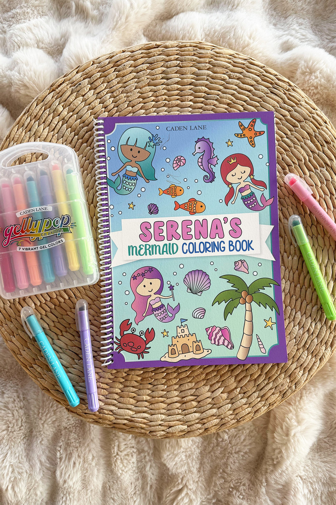 Caden Lane 'Serena's Mermaid Coloring Book' on a woven tray with a fur throw, Gellypop gel crayon case, and pastel Caden Lane markers
