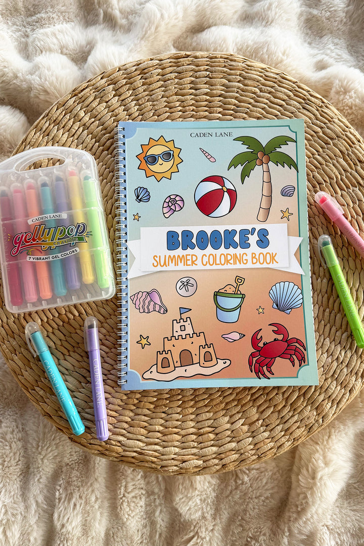 Caden Lane personalized 'Brooke's Summer Coloring Book' on a woven tray with a cream throw, Gellypop gel crayon case, and pastel Caden Lane markers