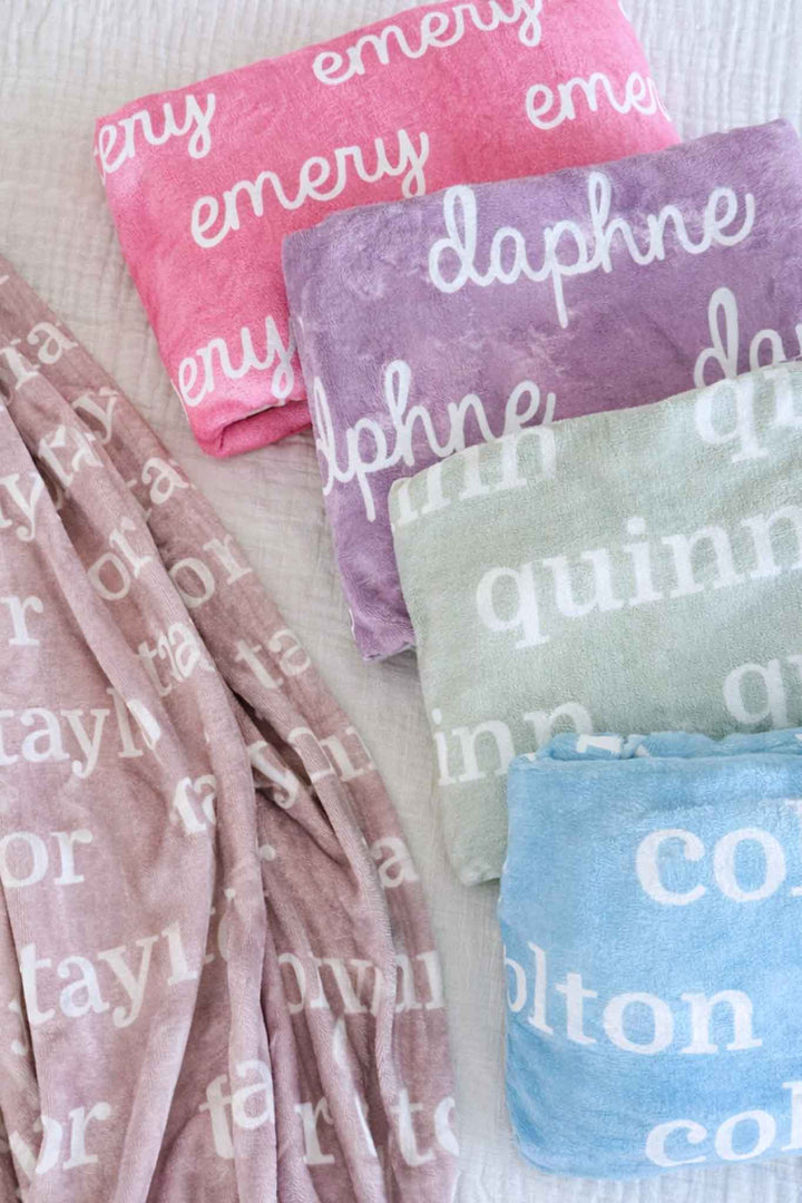 personalized name blankets in pastel colors including taupe, mauvelous pink, violet, basil green, and sky blue