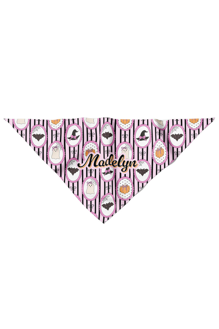 Flat lay of a personalized pink and black striped Halloween pet bandana with pumpkin, bat, and ghost designs, customized with a name in cursive script.