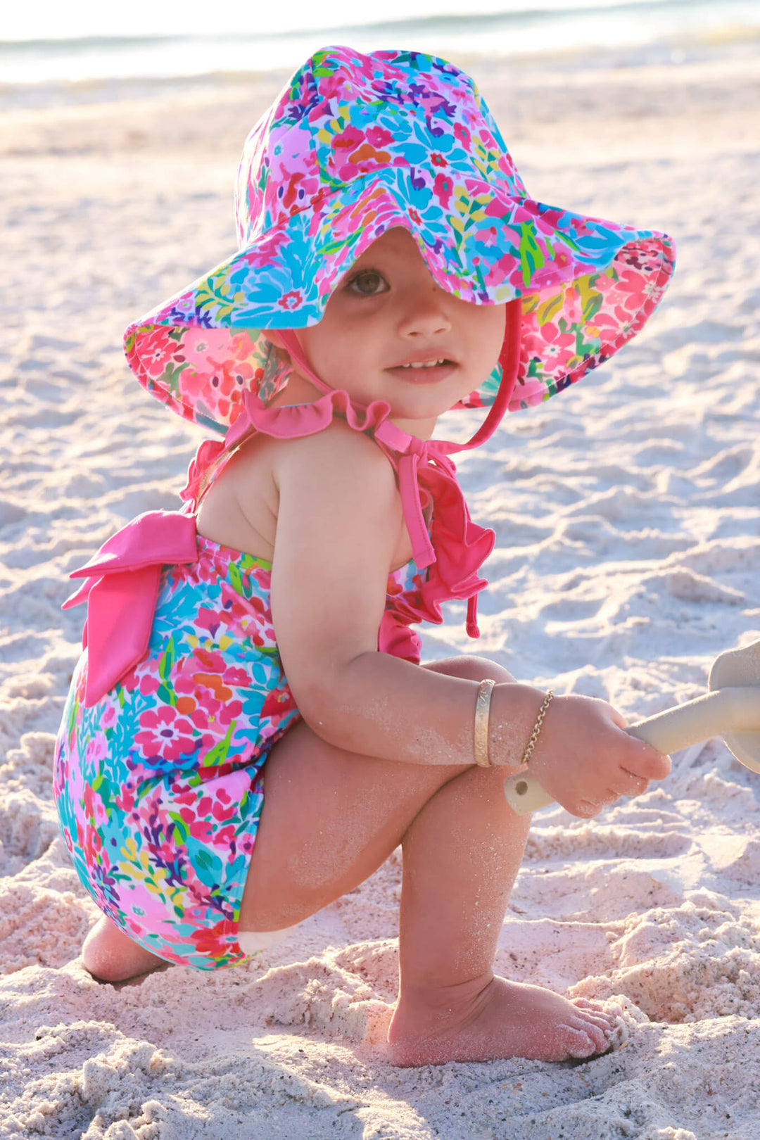 baby girl playing on beach wearing the petal splash double ruffle bow back one piece with the matching sun hat 