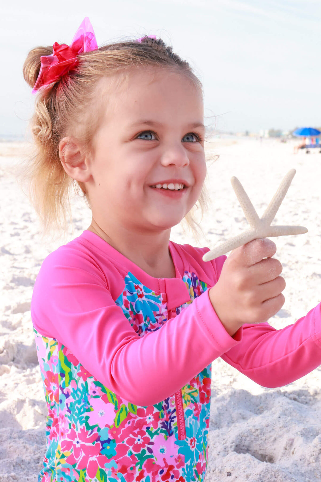 girl playing with star fish on beach in petal splash long sleeve rash guard with front zipper 