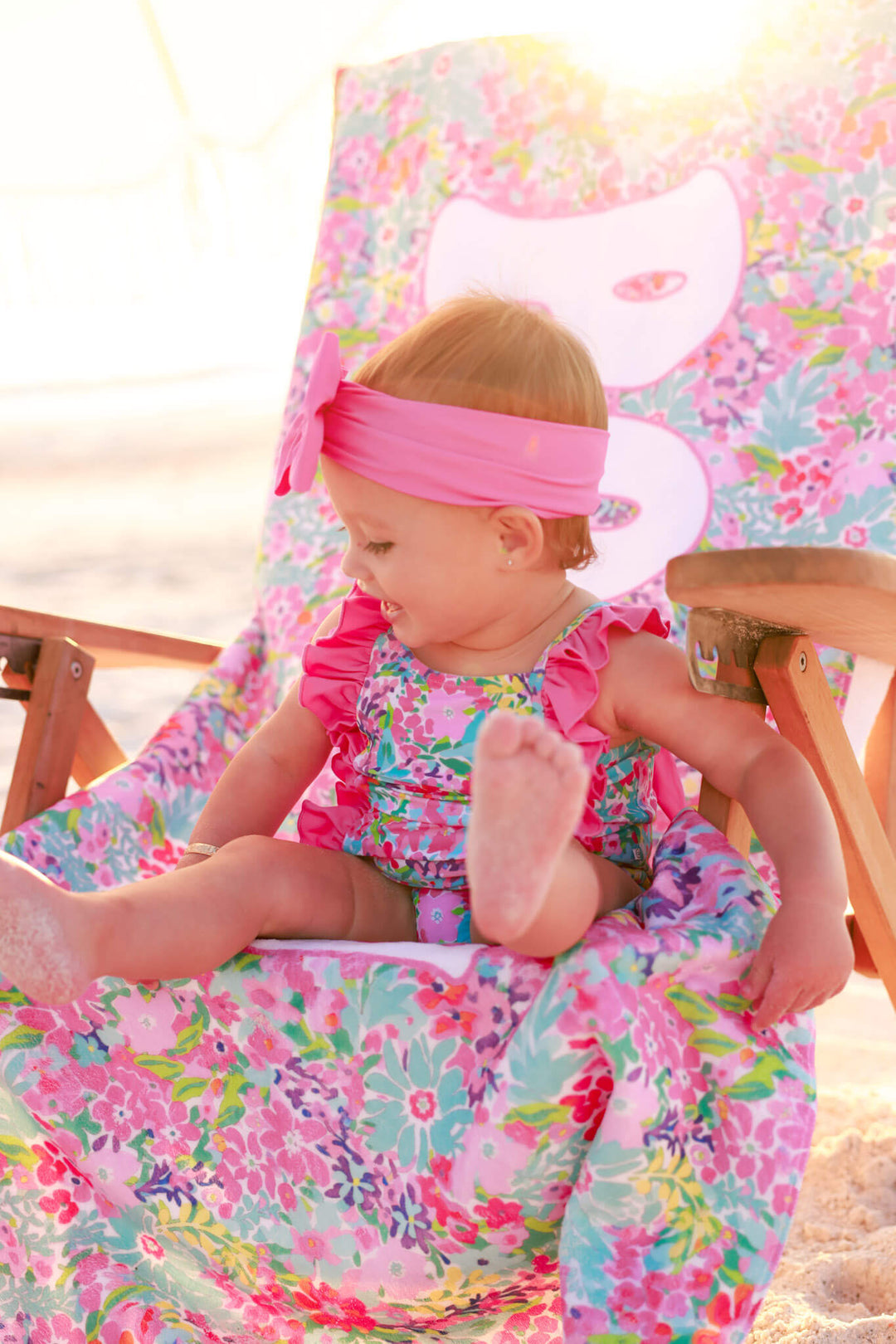 girl sitting on petal splash personalized beach towel draped on beach chair and wearing a matching swimsuit and pink swim bow