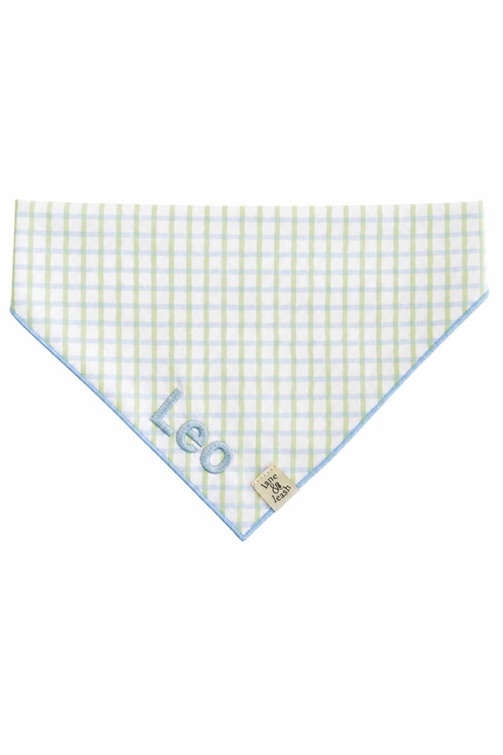 Flat lay of an embroidered pet bandana in green and blue picnic plaid, shown as a triangle with the name "Leo" embroidered on the front