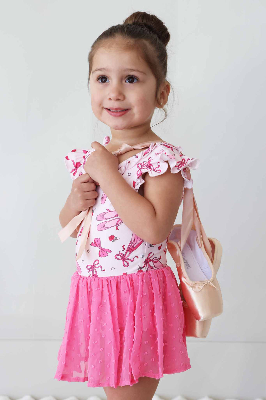 girl holding ballet shoes over her back in pink pirouette leotard 