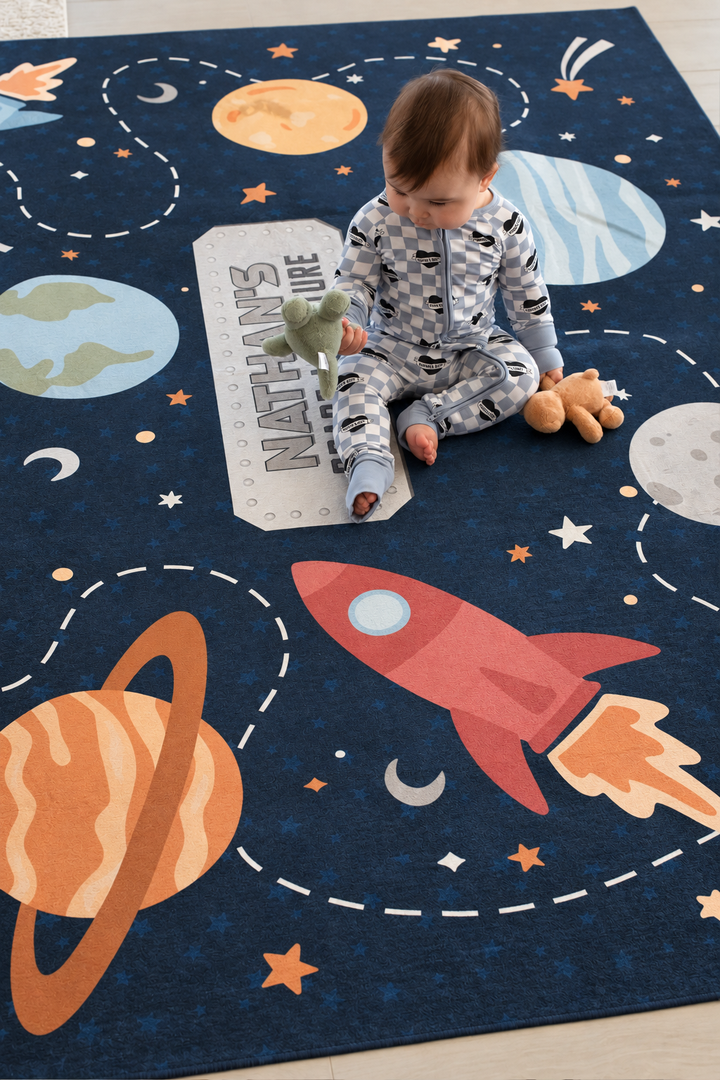 Baby sitting and playing on a personalized Caden Lane space adventure playroom rug featuring rockets, planets and stars.
