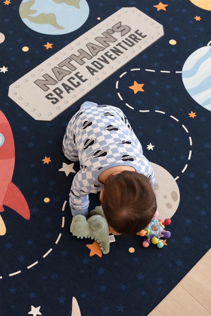 Overhead view of a baby playing on a personalized Caden Lane space-themed kids’ rug with planets, stars and a custom name.