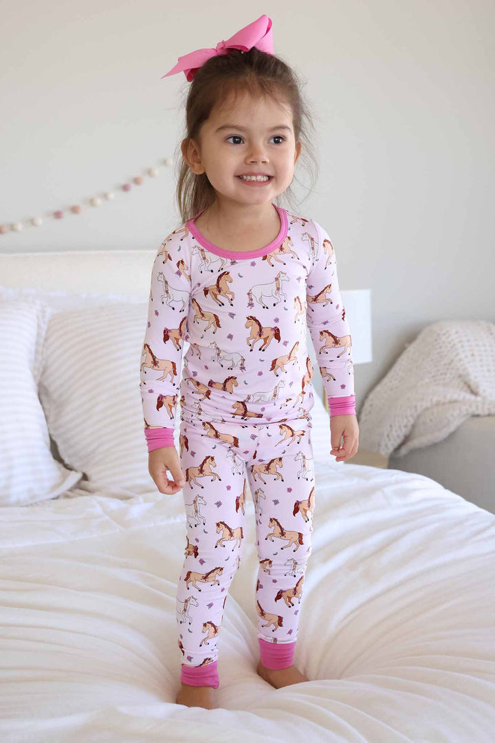 girl standing on bed in pony club pink two piece pajama set 
