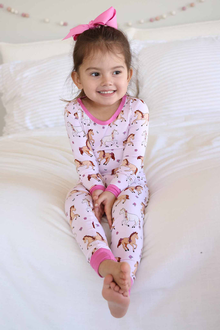 girl sitting on bed in pony club pink two piece pajama set with bright pink clip bow