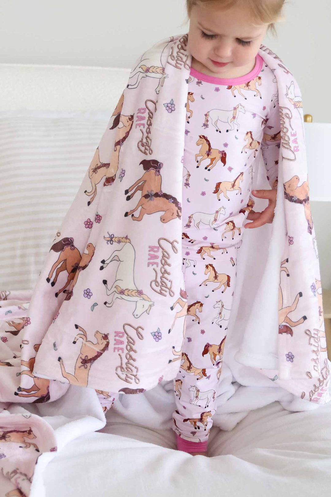girl wearing the pony club pink two piece pajama set with the matching blanket wrapped around her shoulders 