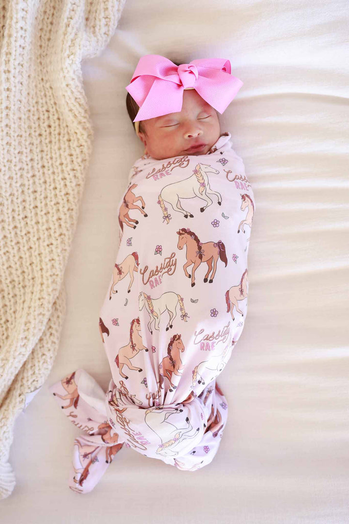 newborn girl with her eyes closed wrapped in the pony club pink personalized swaddle blanket 